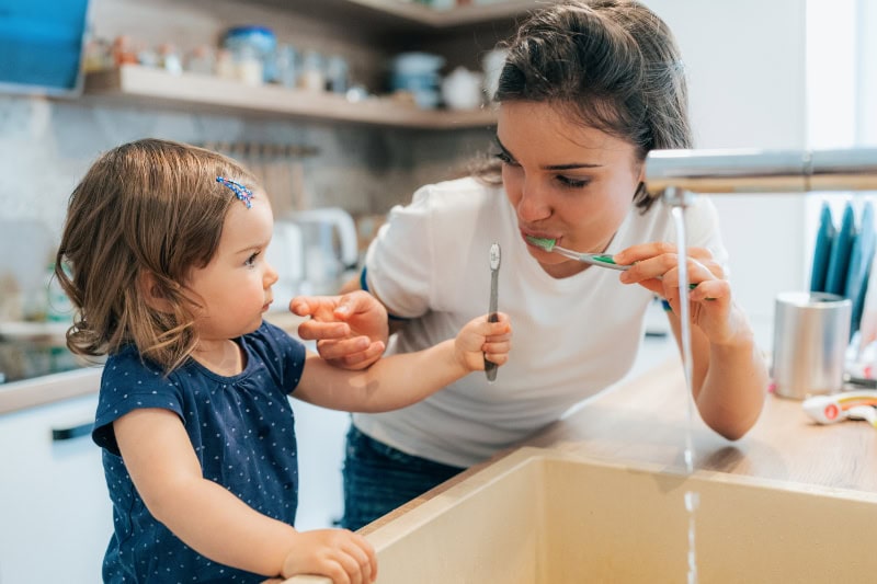 Mother and daughter brushing their teeth together.