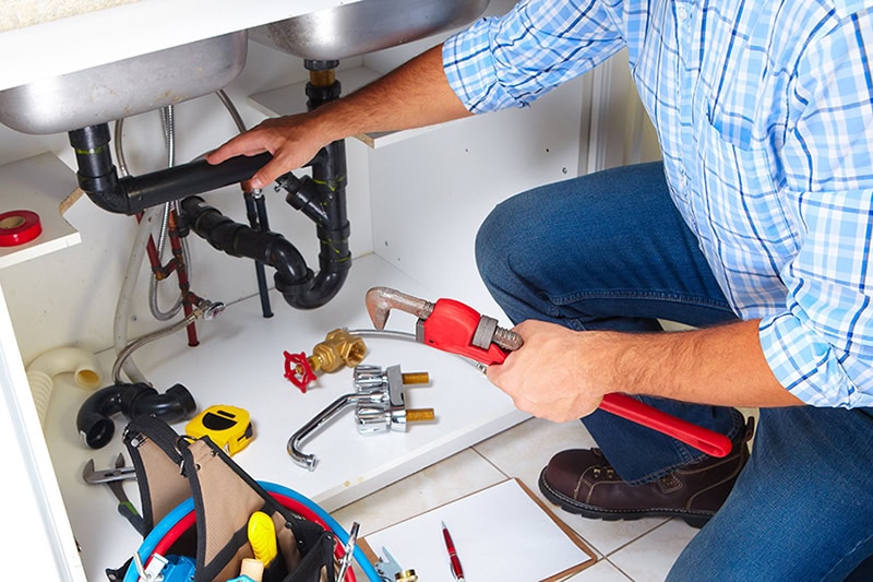 Why You Should Never Ignore Slow-Draining Kitchen Plumbing. Photo of a plumber performing maintenance on a kitchen sink.